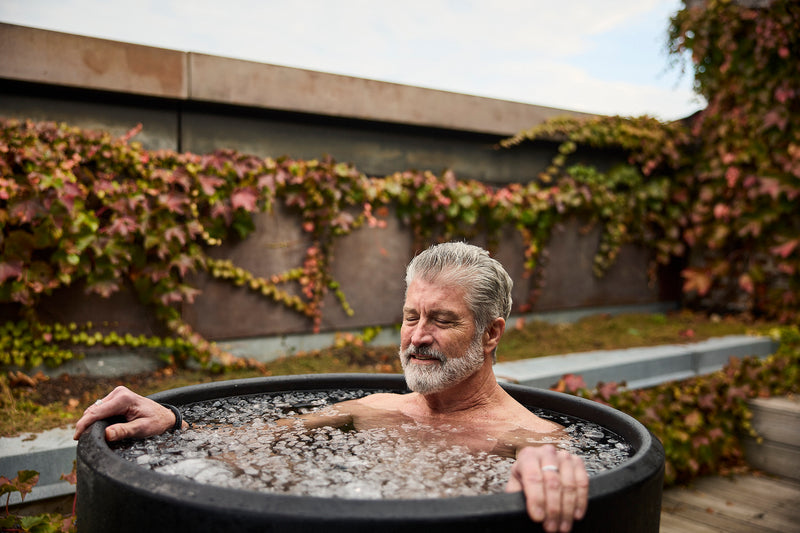 an old man closing his eyes while he's shoulder deep into an ice bath outside in his backyard